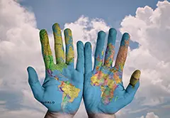 Zwei Hände mit einer daraufgemalten Weltkarte. Im Hintergrund ein blauer Himmel mit Wolken